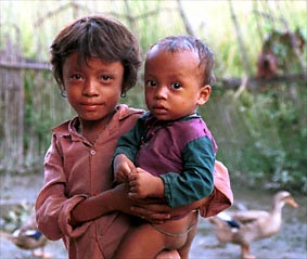 Klein meisje met een baby in een Tharu dorpje, zie de volgende pagina.